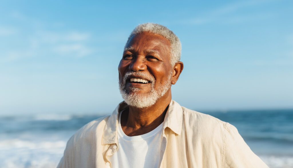 Smiling older man at the beach with an ocean backdrop.